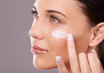 Buy stock photo Studio shot of a beautiful young woman applying a skincare product to her face