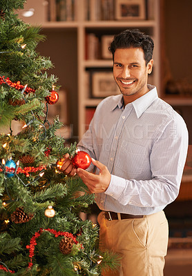 Buy stock photo Shot of a happy young man hanging an ornament on the christmas tree