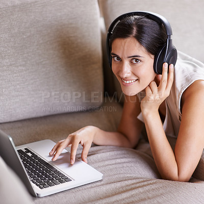 Buy stock photo Shot of a young woman on a sofa wearing headphones and using a laptop