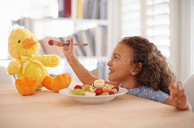 Buy stock photo Child feeding, teddy bear and food at home with happiness and wellness meal with a smile. House, nutrition and young girl with healthy fruit salad and fruits of a hungry kid with toy duck at a table 