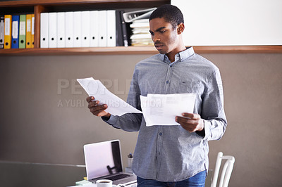 Buy stock photo Shot of a handsome young businessman looking over some paperwork in his home office