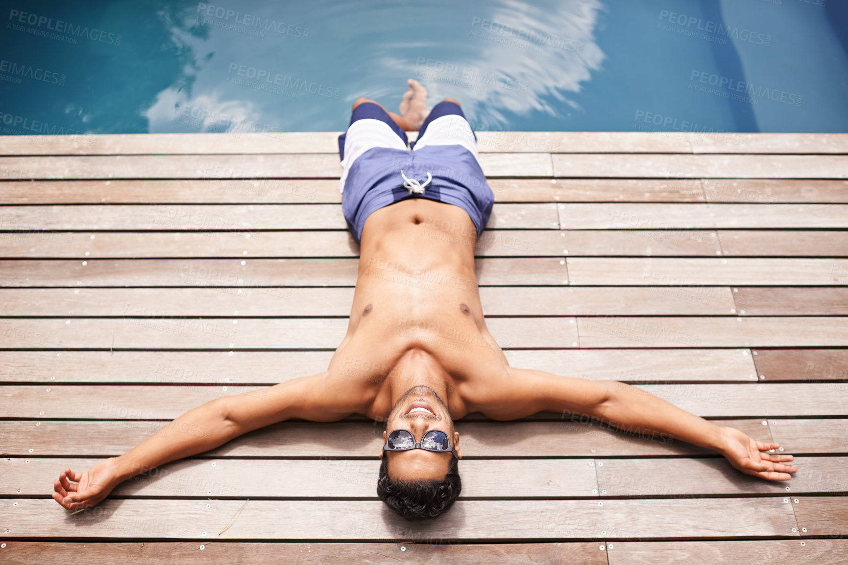 Buy stock photo High angle shot of a young man lying by a pool