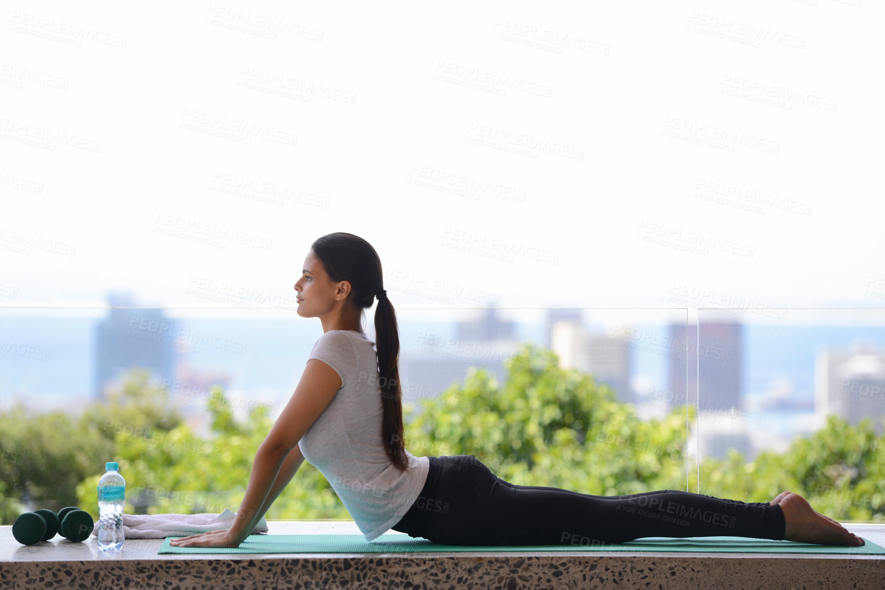 Buy stock photo Shot of a beautiful young woman doing yoga by a window overlooking the city