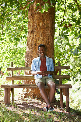 Buy stock photo Teen, boy and portrait on bench outdoors, tree and relax in woods or forest on summer holiday. Black male person, nature and smile in park or sustainable garden, calm and peace on travel to Nigeria