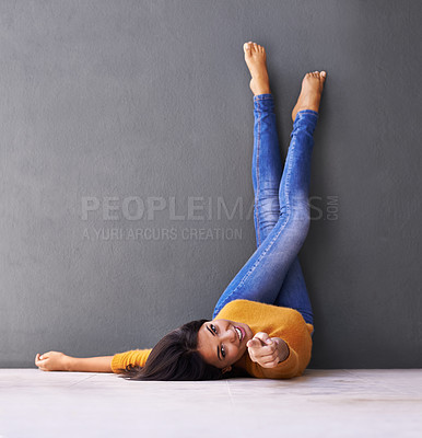 Buy stock photo Woman, smile and wall background for point, feet on wall and relaxing on floor in portrait with fashion. Female person, choice and chill at home for happiness, hey you and wellness in jeans with toes