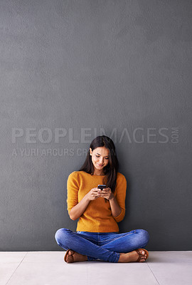 Buy stock photo Shot of an attractive young woman using a mobile phone while sitting on the floor