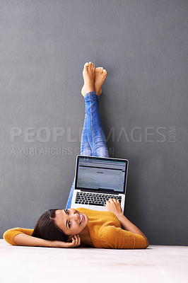 Buy stock photo A young woman lying on the floor with her laptop against a gray background