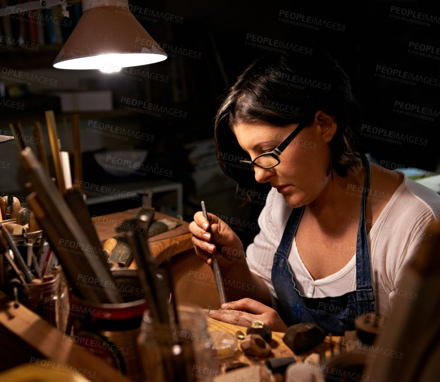 Buy stock photo Carving, wood and artist in workshop with creative project or unique sculpture on table at night. Artisan, carpenter and woman with talent for creativity in dark studio in process of woodworking