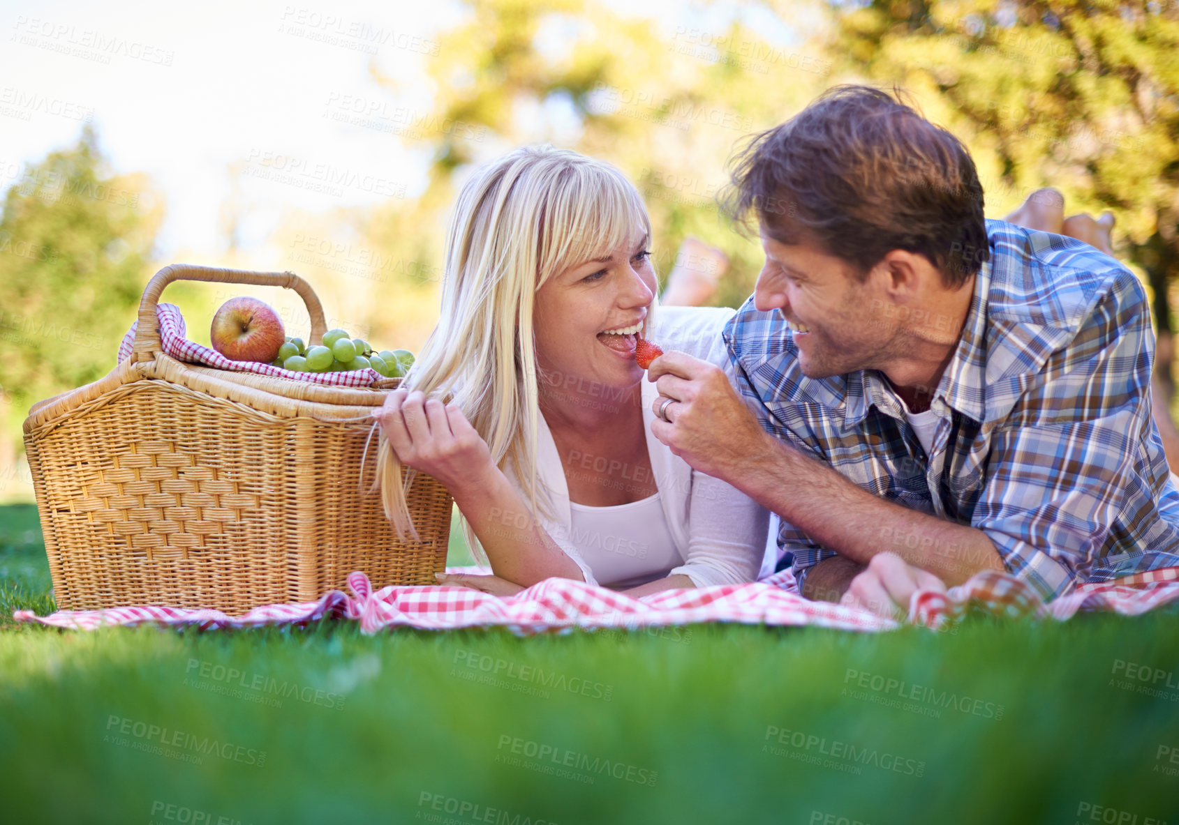Buy stock photo Couple, strawberry and feeding or park picnic as relationship celebration or travel, vacation or happiness. Man, woman and eating fruit in environment for adventure date or snacks, nutrition or love