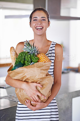 Buy stock photo An attractive woman holding a bag of groceries in the kitchen