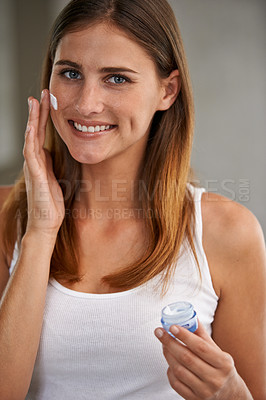 Buy stock photo Portait of an attractive young woman standing in a bathroom applying cream to her face