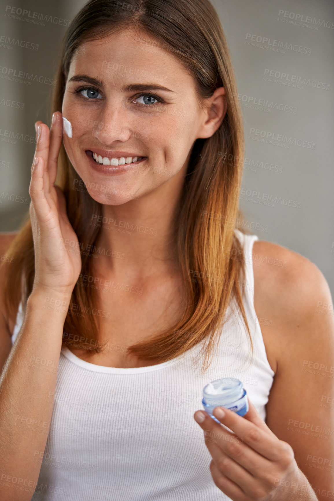 Buy stock photo Portait of an attractive young woman standing in a bathroom applying cream to her face