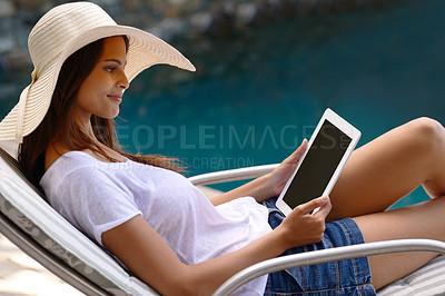 Buy stock photo Shot of an attractive young woman using a digital tablet by the poolside