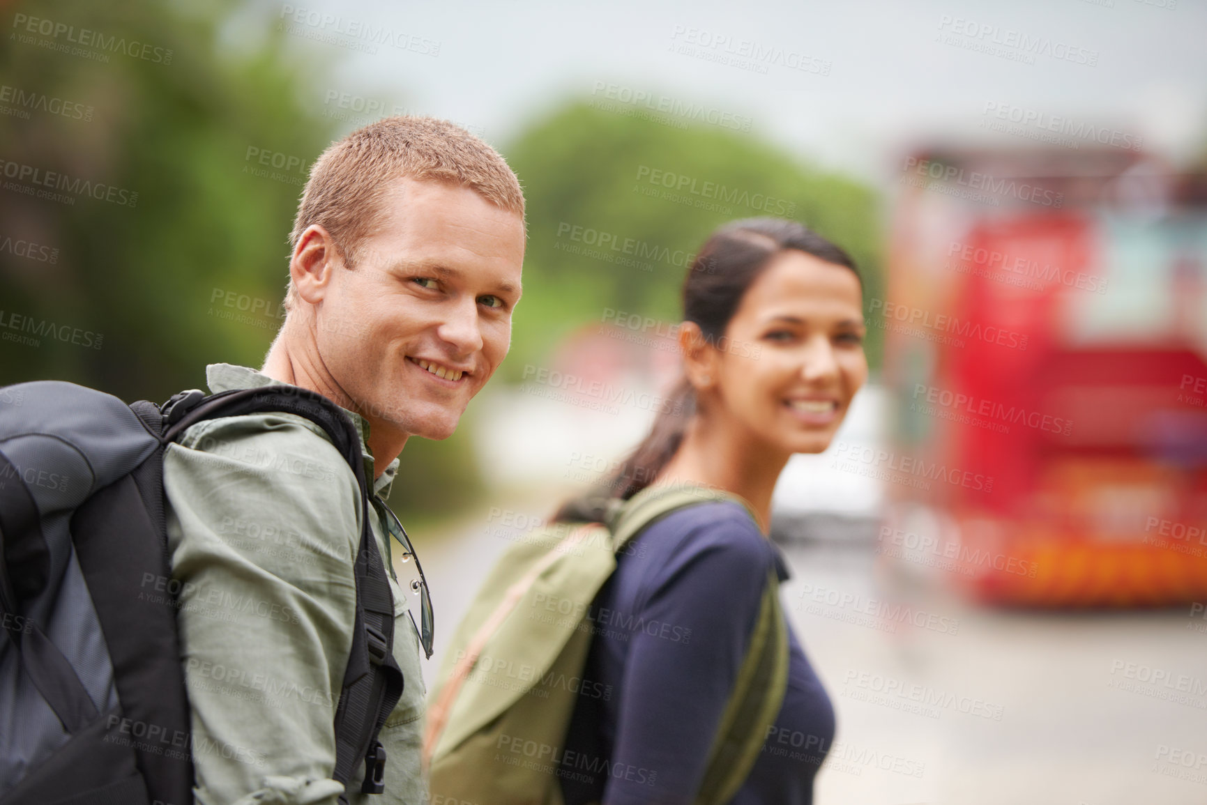Buy stock photo A travelling couple smile at the camera while waiting for their bus to arrive