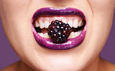 Buy stock photo Woman lips, purple lipstick with berry and makeup, shine and creativity with beauty isolated on studio background. Closeup of fruit between female model teeth, cosmetic product and cosmetology