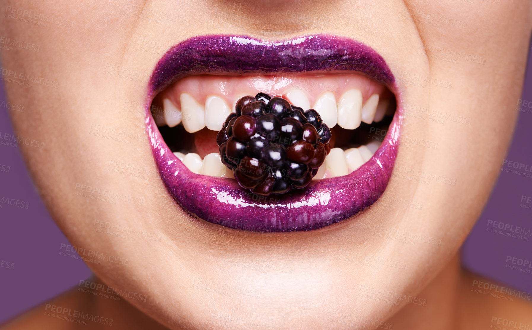 Buy stock photo Woman lips, purple lipstick with berry and makeup, shine and creativity with beauty isolated on studio background. Closeup of fruit between female model teeth, cosmetic product and cosmetology