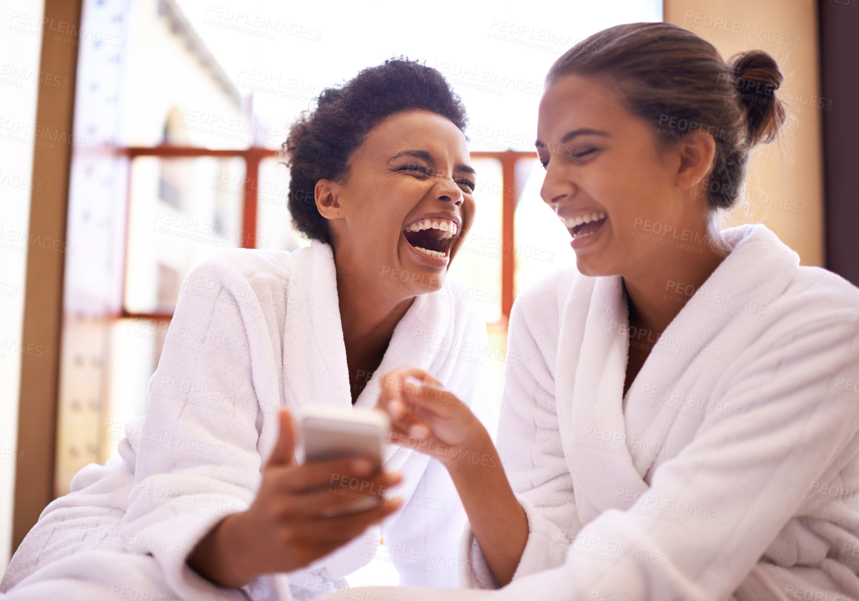 Buy stock photo Beauty, phone and spa with women laughing in robes for luxury pampering or treatment together. Happy, app and social media with funny young friends at resort or salon for wellness or weekend getaway