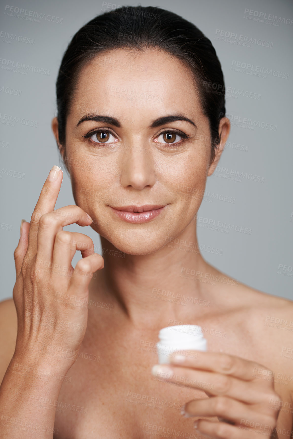 Buy stock photo Portrait, woman and apply cream for skincare in studio isolated on a gray background. Face, cosmetics and mature model with moisturizer in container for dermatology, beauty or hydration for antiaging