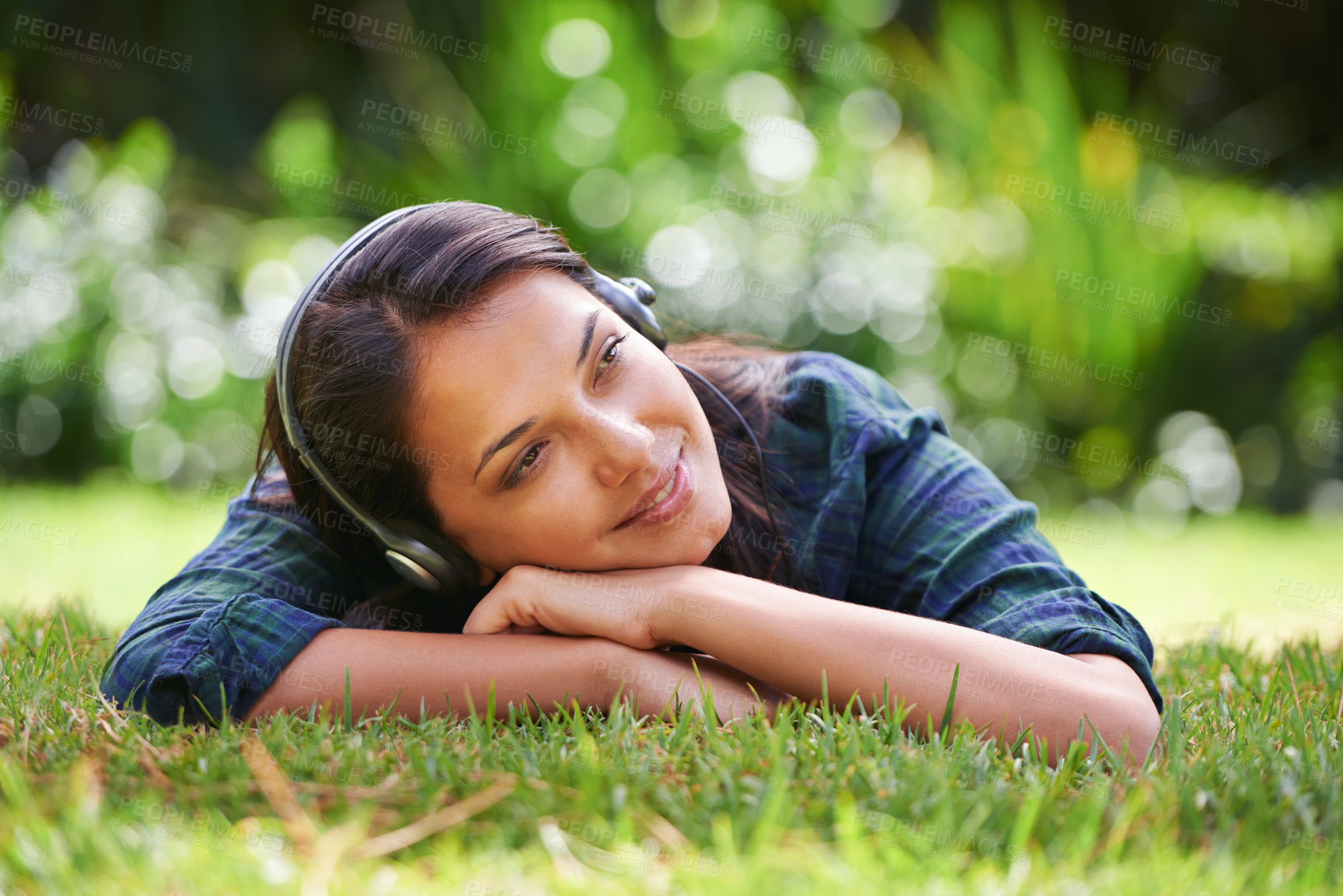 Buy stock photo Shot of an attractive young woman lying on the grass and listening to music
