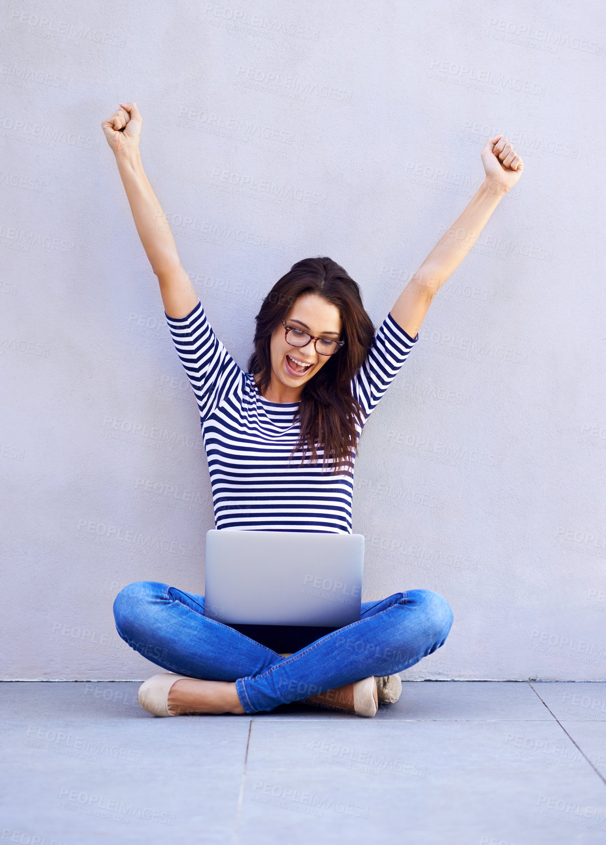 Buy stock photo A young woman raising her arms in celebration while looking down at the screen of her laptop