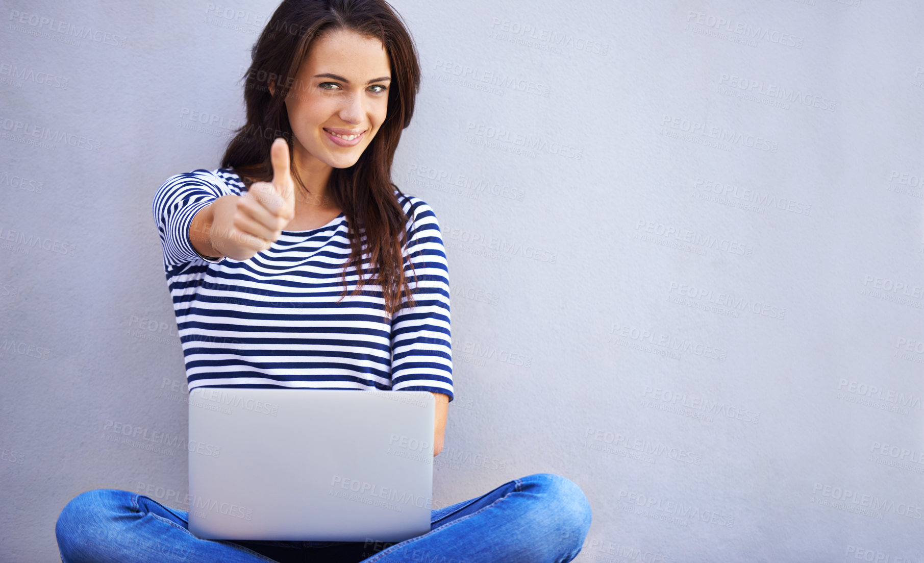 Buy stock photo An attractive young woman showing the thumbs up sign while sitting with her laptop