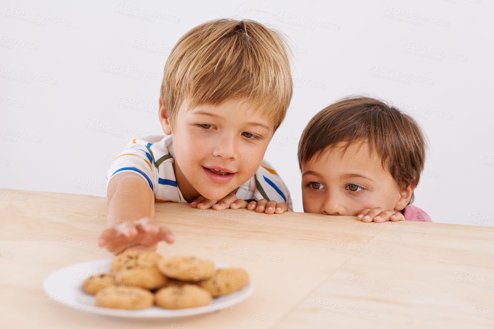 Buy stock photo Children, boys and smile for cookies in home with stealing, peeking and childhood fun in at dining room table. Siblings, kids and happy for biscuits, snack and baked goods in kitchen of apartment