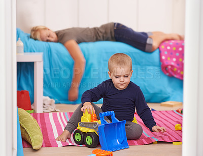 Buy stock photo A toddler playing with his toys while his mom naps on his bed