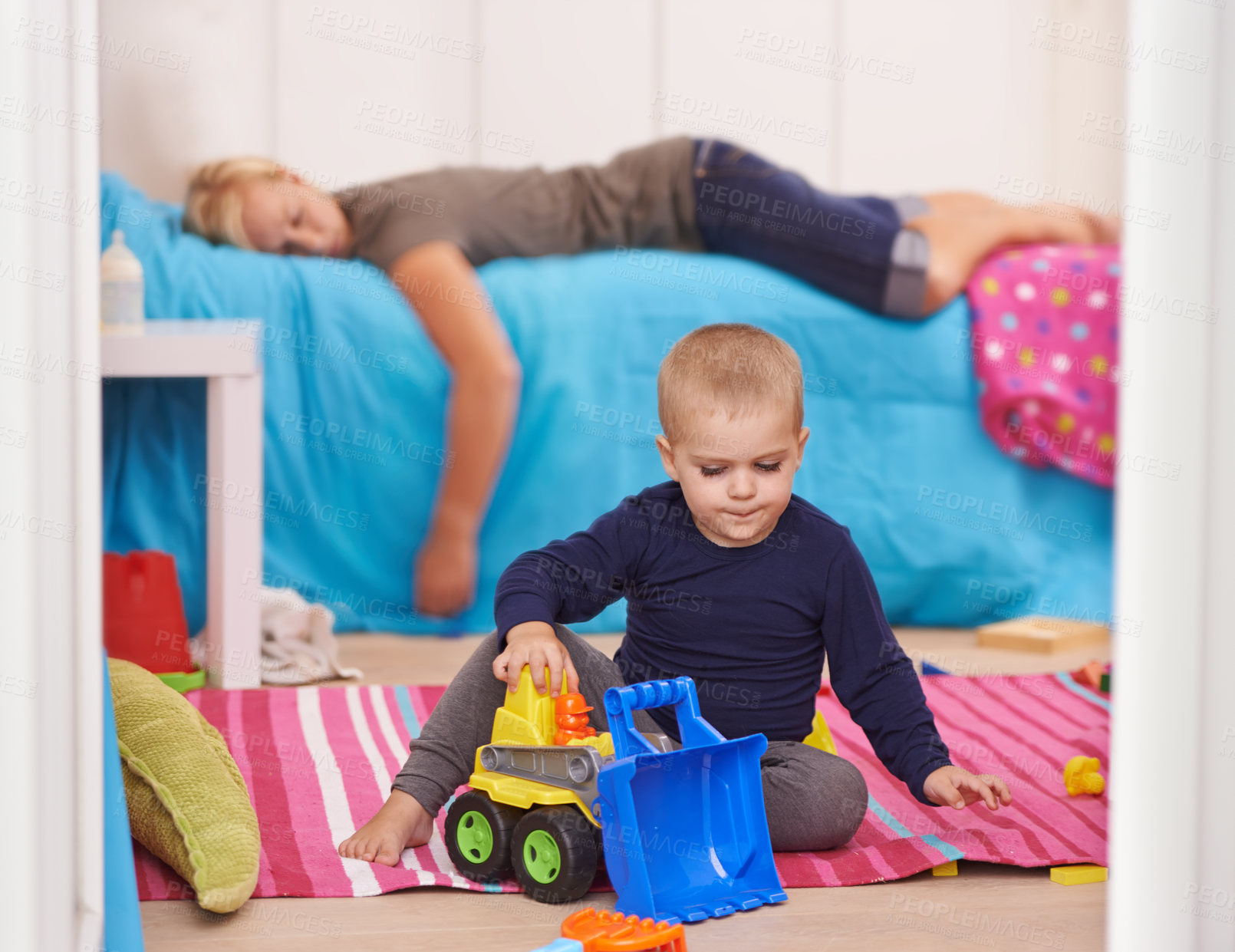 Buy stock photo A toddler playing with his toys while his mom naps on his bed