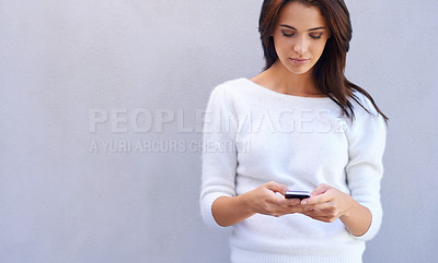 Buy stock photo Shot of an attractive young woman standing against a gray background and using her mobile phone