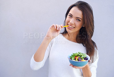 Buy stock photo Portrait of an attractive young woman standing against a gray background and eating a bowl of salad
