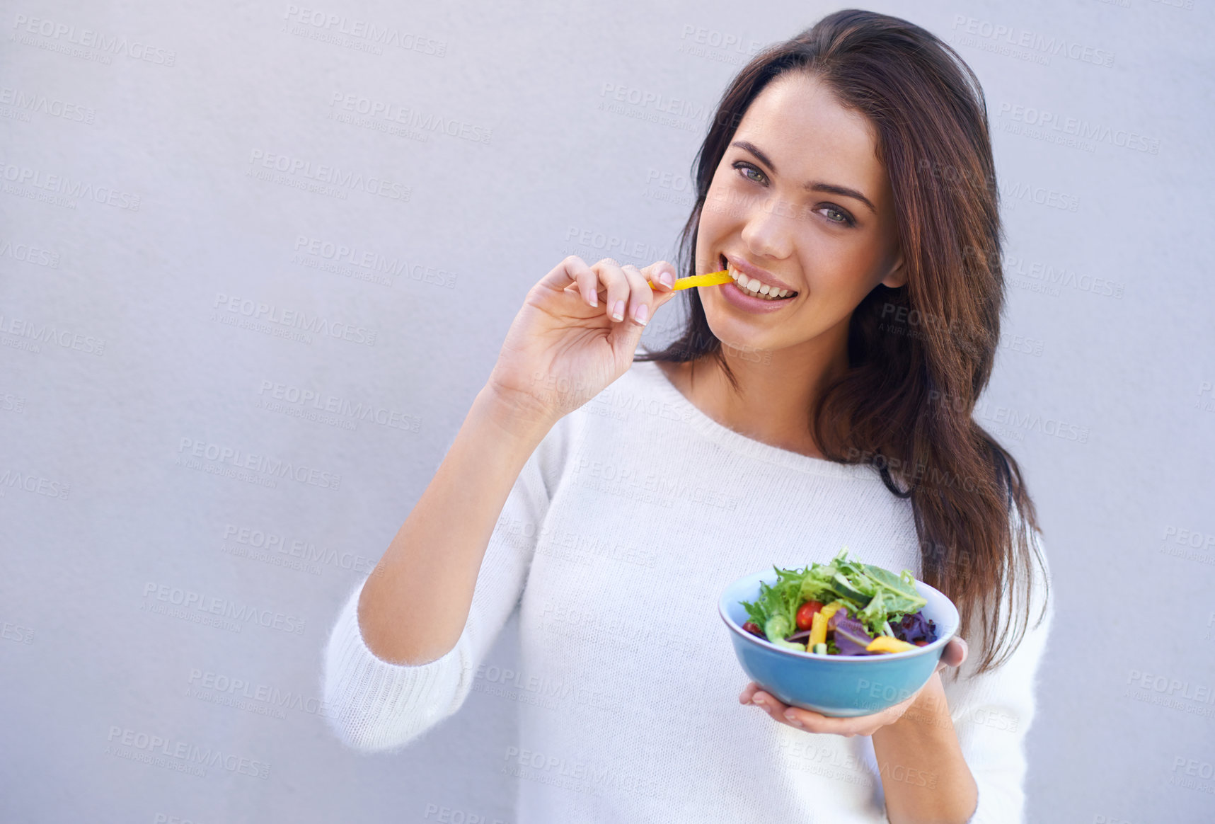 Buy stock photo Portrait of an attractive young woman standing against a gray background and eating a bowl of salad