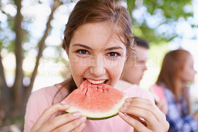 Buy stock photo Portrait, teenager and girl bite of watermelon with friends in background in morning for breakfast. Spring, outdoor and female person in park with classmates for picnic, eating fruit as healthy food