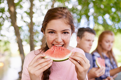 Buy stock photo Portrait, teenager and girl eating watermelon with friends in background in morning for breakfast. Spring, outdoor and female person in park with classmates for picnic to eat fruit as healthy food