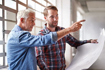 Buy stock photo Shot of two male architects holding blueprints inspecting a building