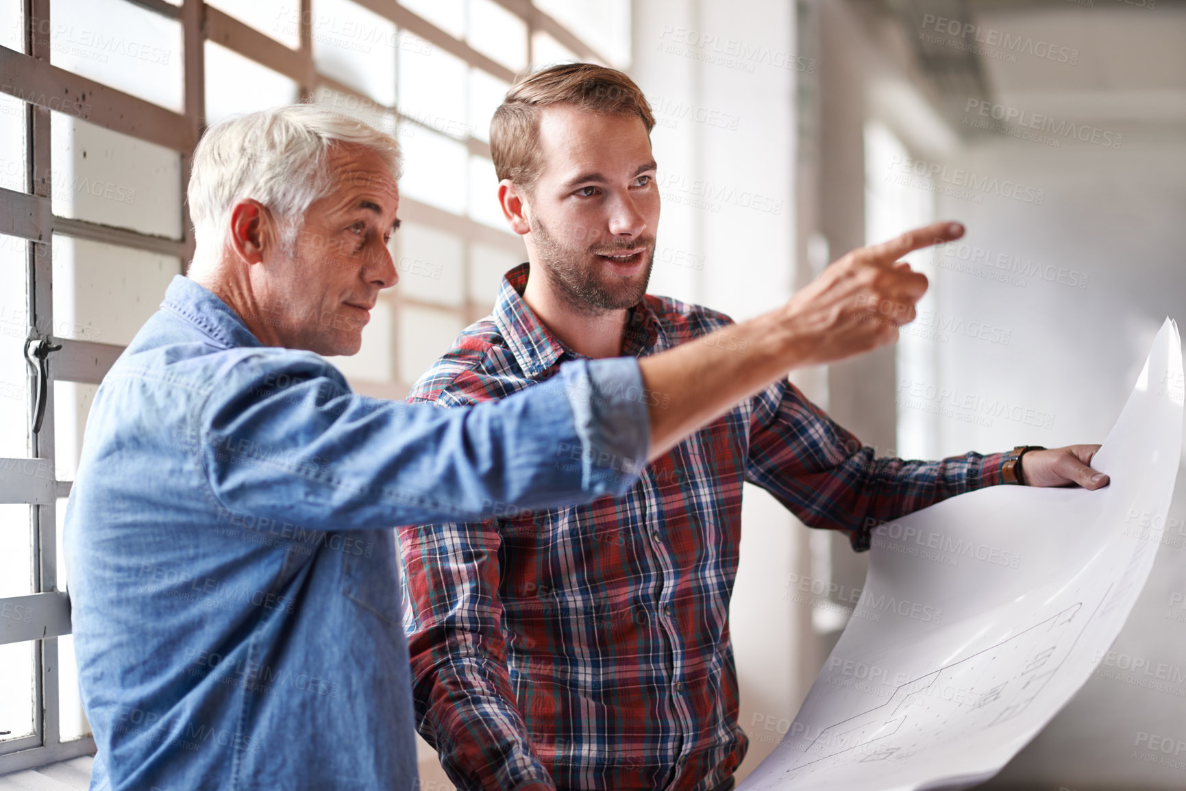 Buy stock photo Shot of two male architects holding blueprints inspecting a building