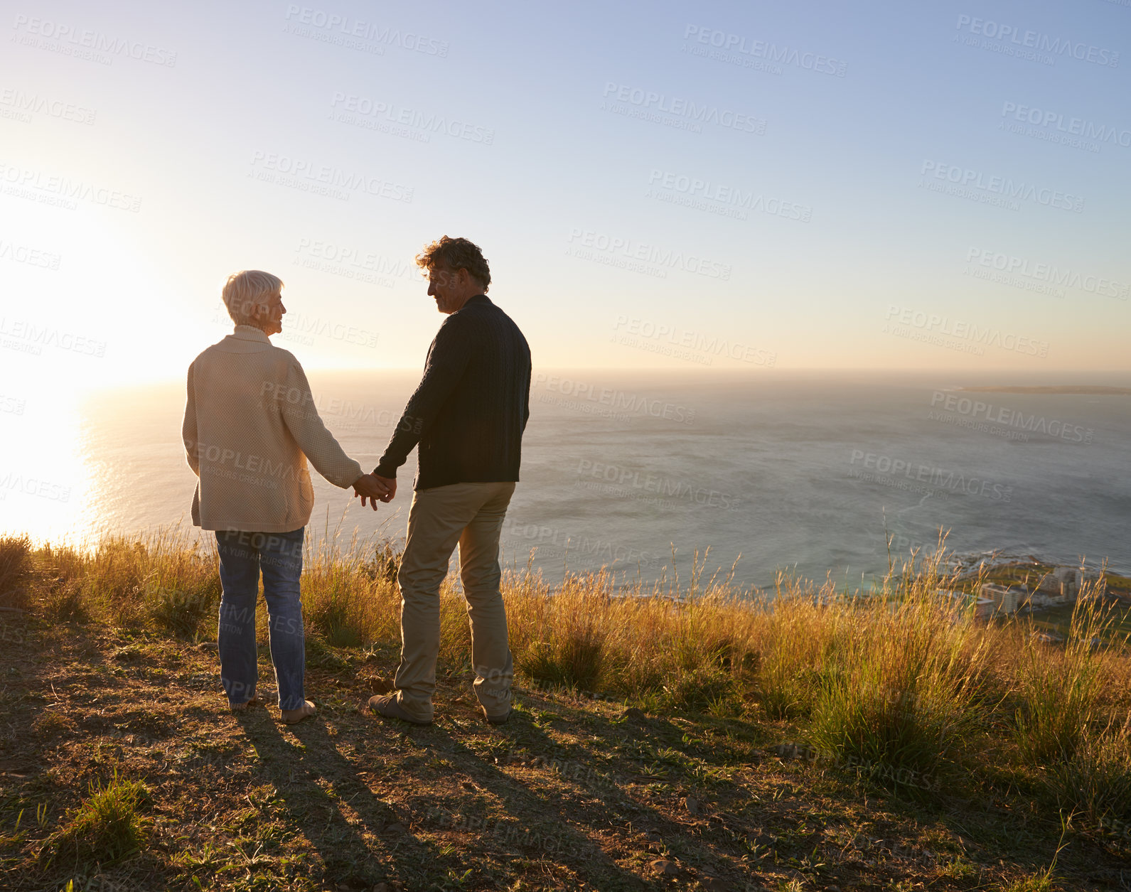 Buy stock photo Happy, vacation and couple holding hands at sunset in nature, outdoor on hill or mountain in Cape Town. People, love and support with kindness on holiday adventure in countryside and relax together