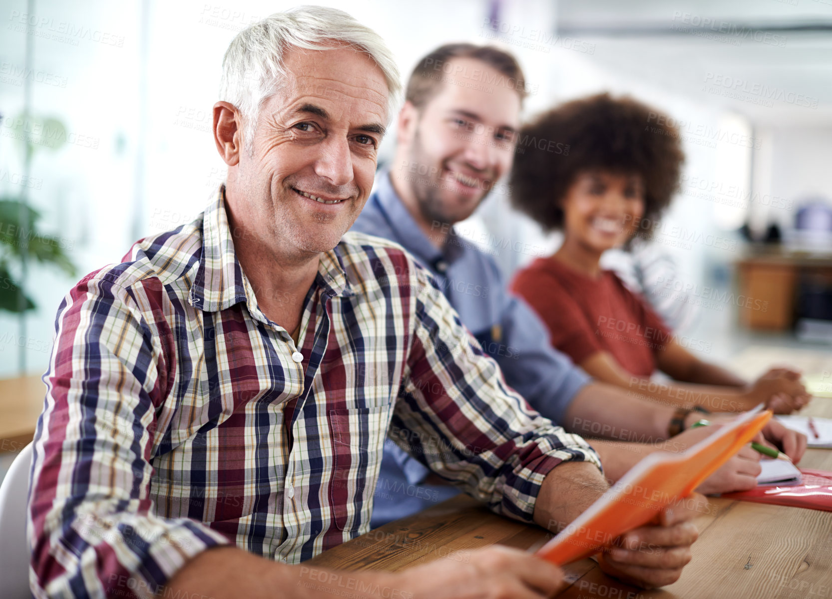 Buy stock photo Portrait of an attractive mature businessman seated with his colleagues at a table