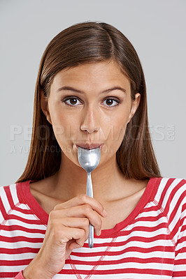 Buy stock photo Studio shot of an attractive young woman with a spoon in her mouth on a grey background