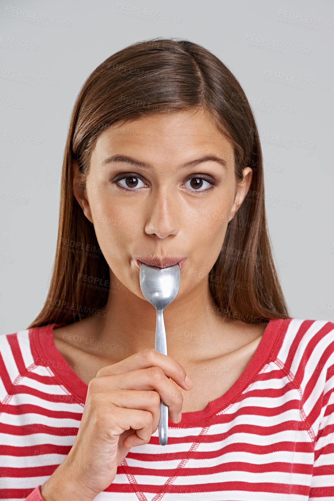 Buy stock photo Studio shot of an attractive young woman with a spoon in her mouth on a grey background