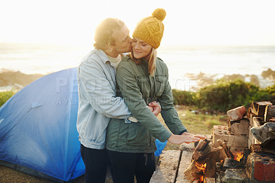 Buy stock photo Happy couple, kiss and bonding together by campfire, outdoor and romantic getaway with camping in forest. Man, woman and love on vacation on weekend break, countryside and travel in woods for sunset