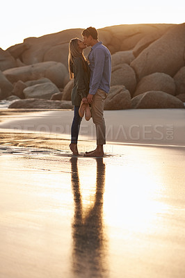 Buy stock photo Shot of a young couple enjoying a romantic kiss on the beach at sunset