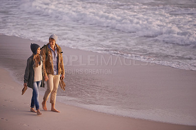 Buy stock photo Shot of a young couple enjoying a romantic stroll on the beach