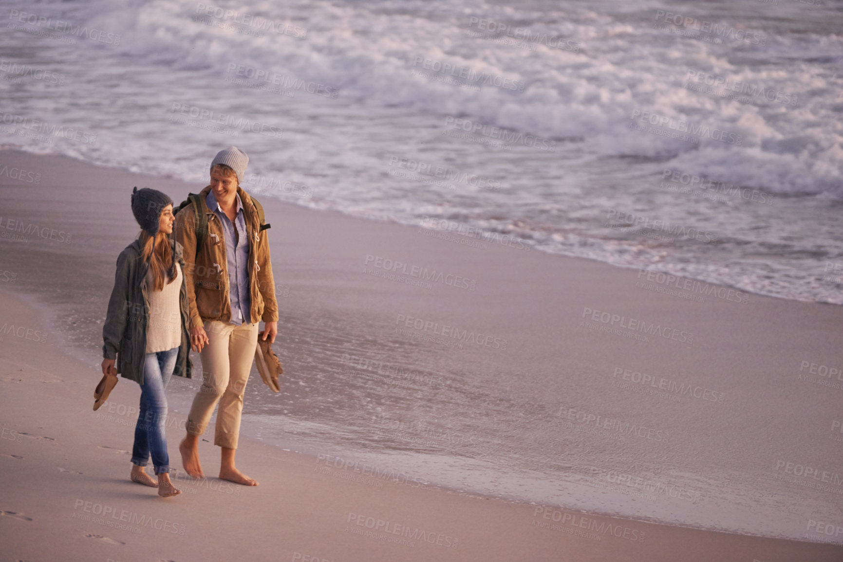 Buy stock photo Shot of a young couple enjoying a romantic stroll on the beach