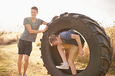 Buy stock photo Boys, farm and playing with tyre in nature for summer camp, exercise and holiday enjoyment. Teenager, smile and happy with wheel for vacation, fun game and summer holiday together in Australia