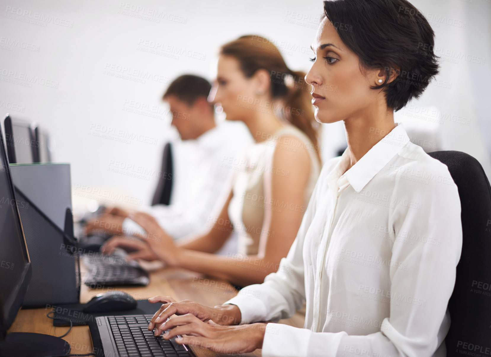 Buy stock photo Shot of an attractive young office worker at her computer with her colleagues in the background