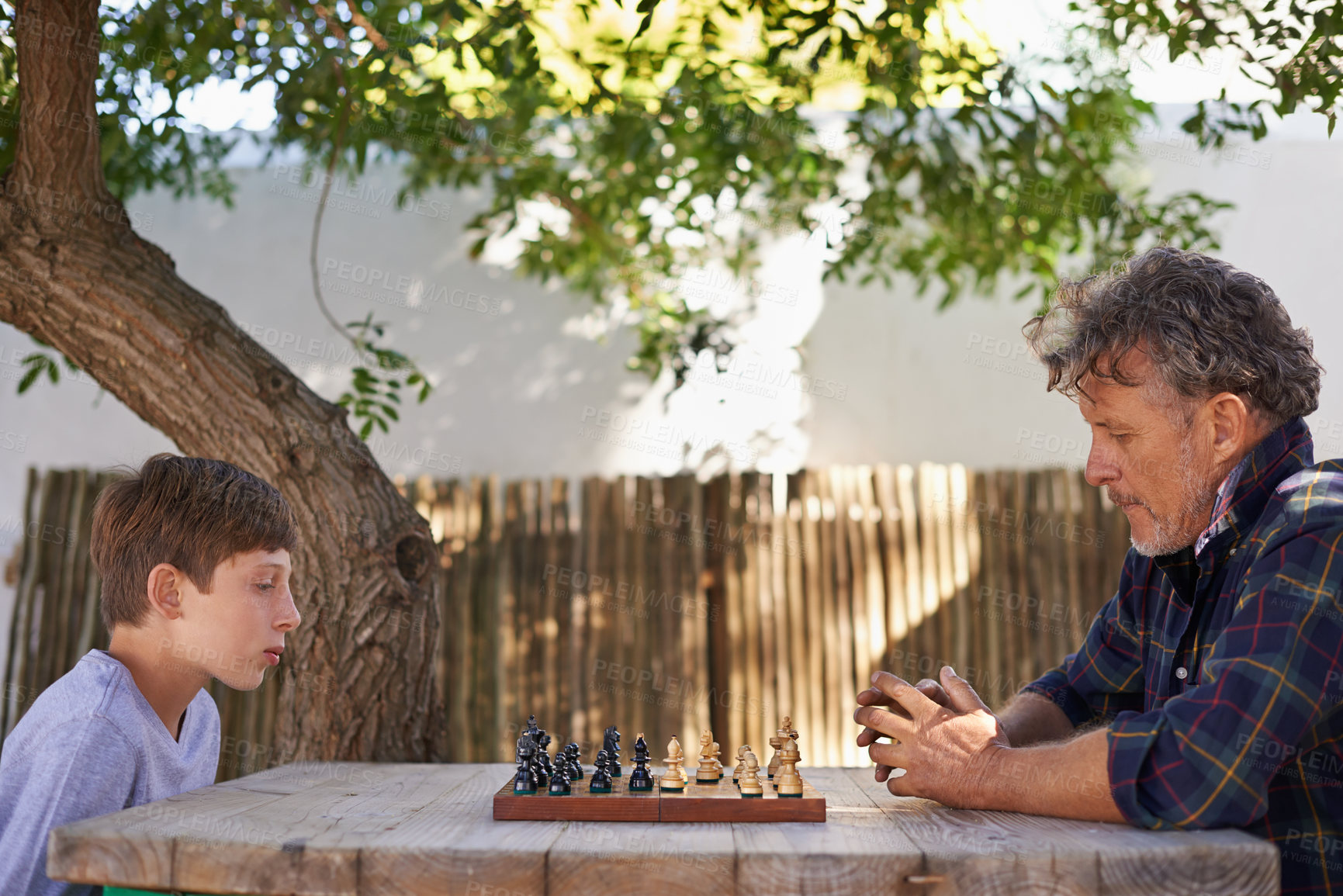 Buy stock photo Mature man, boy and chess with game outdoor, strategy and skill with focus in garden for bonding. Grandfather, child and family fun in backyard with boardgame, competition and concentration for move
