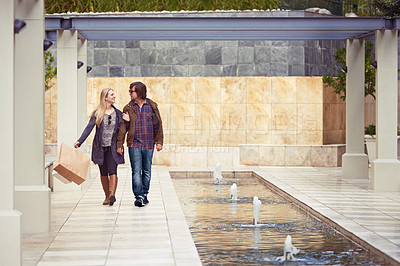 Buy stock photo An affectionate young couple walking under a pergola next to a water feature