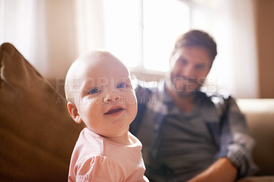 Buy stock photo Shot of an adorable baby girl sitting on the sofa with her father in the background