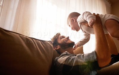 Buy stock photo Funny, dad and lifting baby on sofa in home living room, playing or bonding together. Happy, care and father holding infant, newborn or child on couch in lounge, having fun and enjoying quality time.