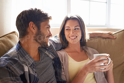 Buy stock photo Coffee, love and couple smiling at each other or on a couch in the living room or bonding and conversation. Man, woman and communicating or affectionate with hot beverages or happy partners at home